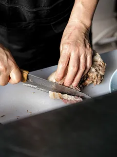Person slicing meat on wooden cutting board with knife