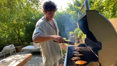 Man grilling chicken on barbecue in backyard on sunny day